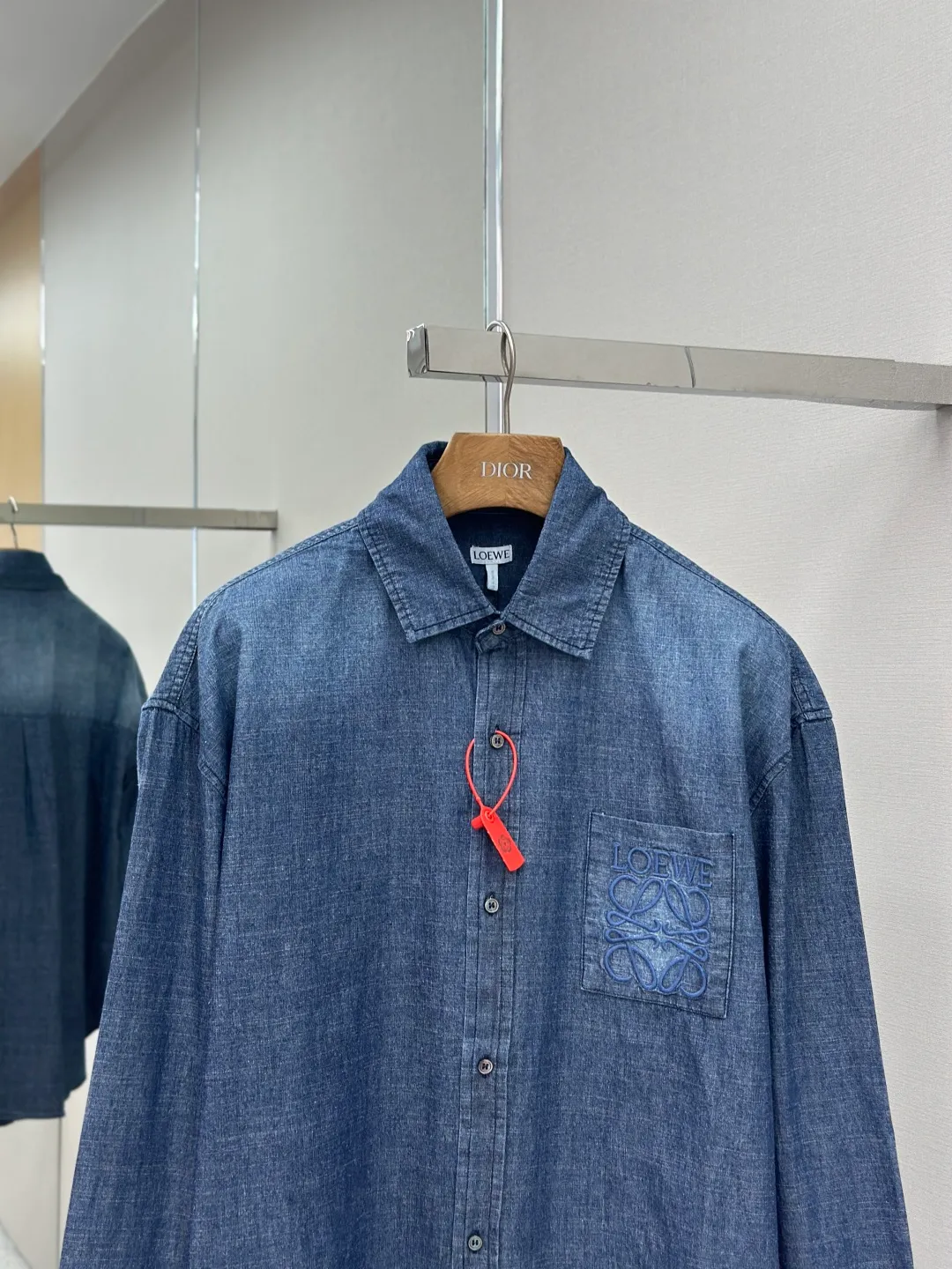 P430 Loewe Anagram Gradient Embroidered Pocket Shirt Made of custom-made high-quality cotton chambray fabric, with a unique washed gradient blue as the main tone, from dark to light and from thick to light. The chest patch pocket is decorated with Loewe Anagram embroidery as its soul, engraved with LOEWE-style casual elegance, and the natural and smooth lines show the casualness.  Imported embroidery machines are used, and advanced computer control systems and precision mechanical components are used to realize Loewe embroidery operations.  The gradient dynamic spray dyeing process uses specialized spray dyeing equipment to accurately spray dye onto the surface of the fabric in the form of mist (by accurately controlling the different dimensions of the spray of the spray dyeing equipment, combined with the movement speed and direction during the dyeing process) to present a smooth and natural transition effect of color. The butterfly rhyme pinch pleating body dart technology is inspired by the beautiful shape of butterflies, and uses precise pinch pleating techniques to create a flexible pleat effect like butterfly wings on the garment, making the garment fit more closely to the body.  size:44.46.48.50
